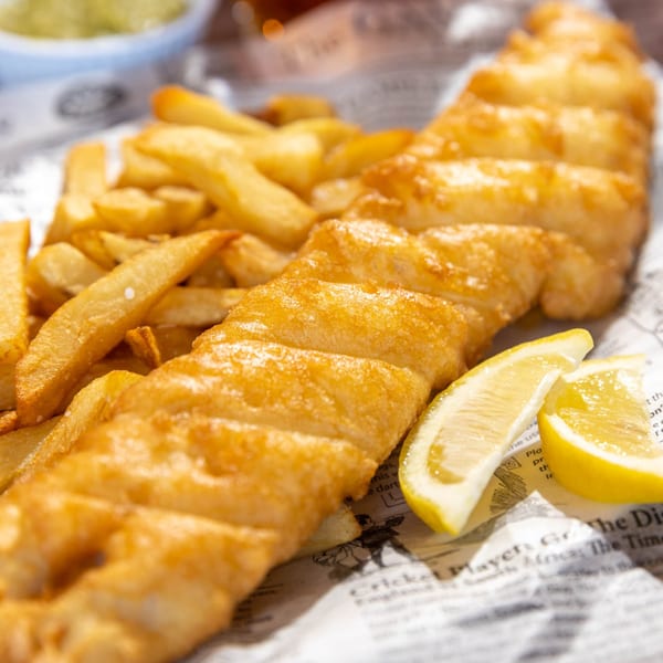 Golden-brown fish and chips with lemon wedges, served on newspaper-print paper.