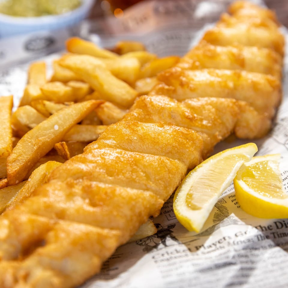 Golden-brown fish and chips with lemon wedges, served on newspaper-print paper.