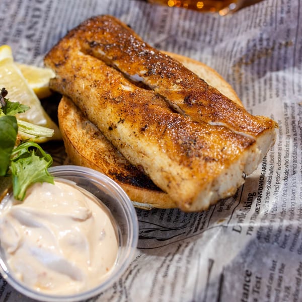 Go Brit! fish sandwich with toasted bread, lemon wedges, and a side of sauce.