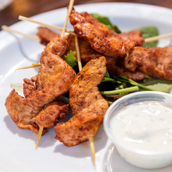 Grilled chicken skewers with a side of creamy white sauce and green garnish on a white plate.