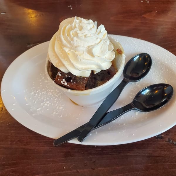 A British sticky toffee pudding with whipped cream and two black spoons on a white plate.