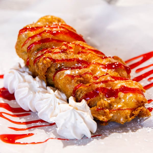 Deep-fried dessert drizzled with red sauce and powdered sugar, served with white meringue dollops.
